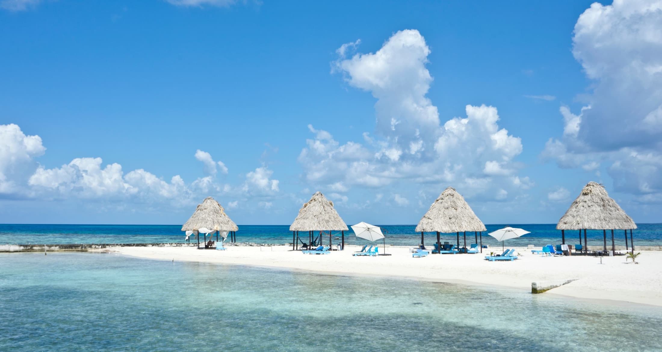 Thatched palapas on a white-sand caye over the turquoise waters of Belize